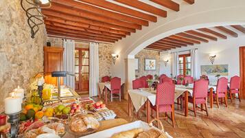 A dining area with a stone wall, wooden beams, and red upholstered chairs.