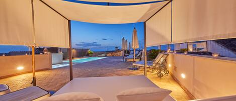 A rooftop terrace with a pool, lounge chairs, and umbrellas.