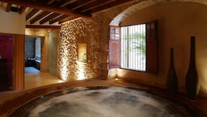 A spa area with a hot tub, stone walls, wooden beams, and a window with bars. - Cas Comte Suites & Spa - Adults Only (Lloseta)