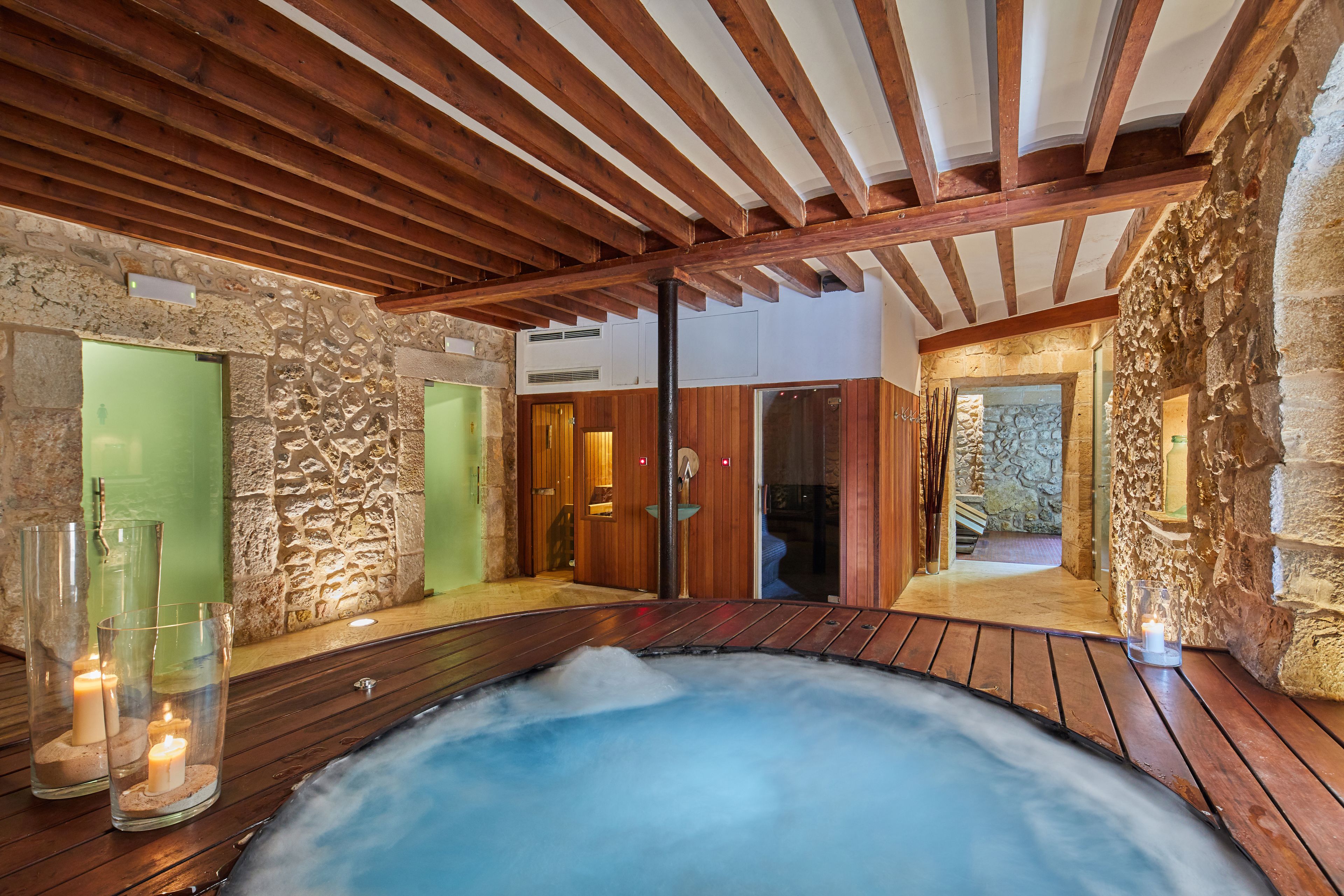 Un área de spa con terraza de madera, un jacuzzi, paredes de piedra y puertas de madera.