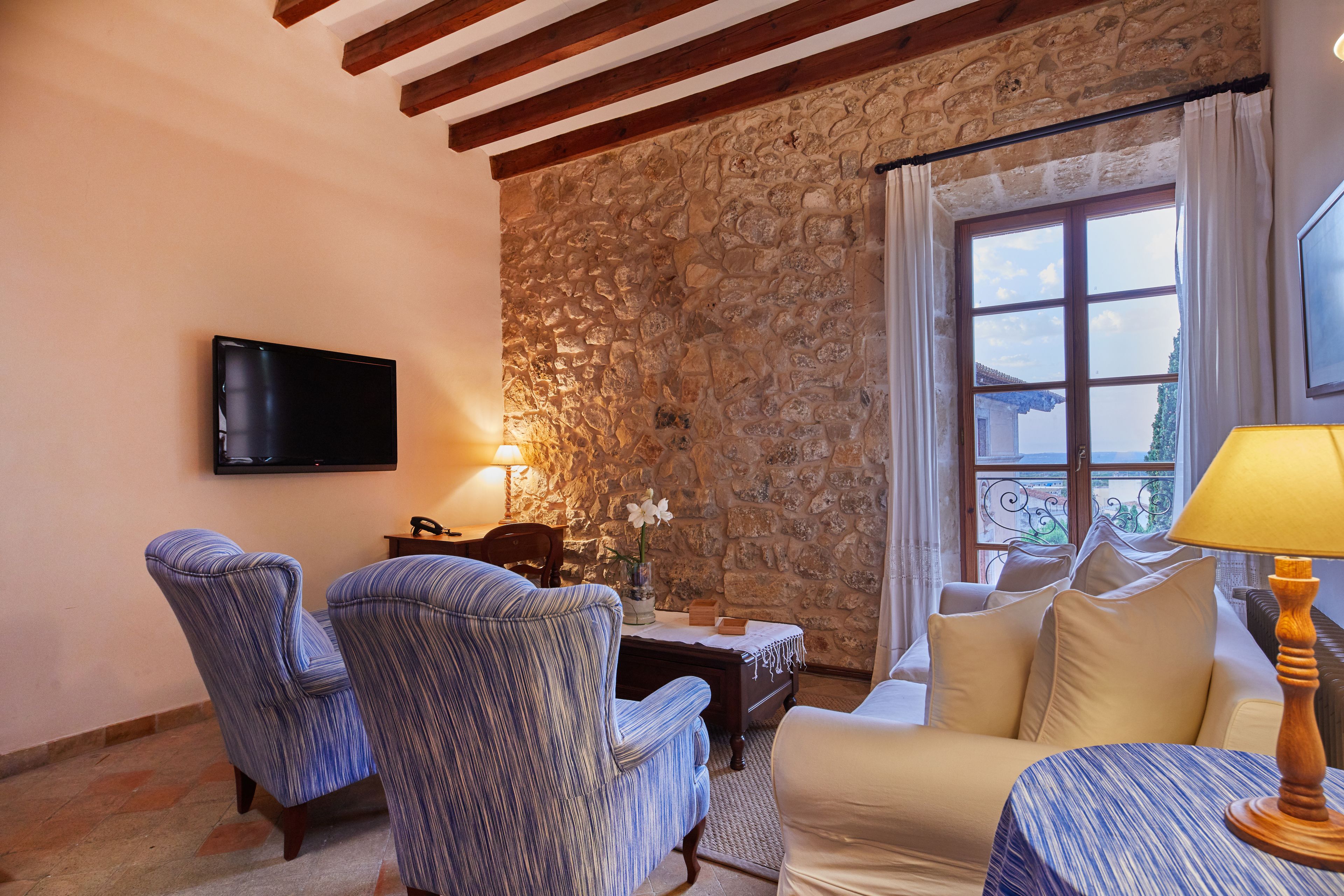 A cozy living room with a stone wall, a flat-screen TV, striped armchairs, a sofa, and a table with a lamp.