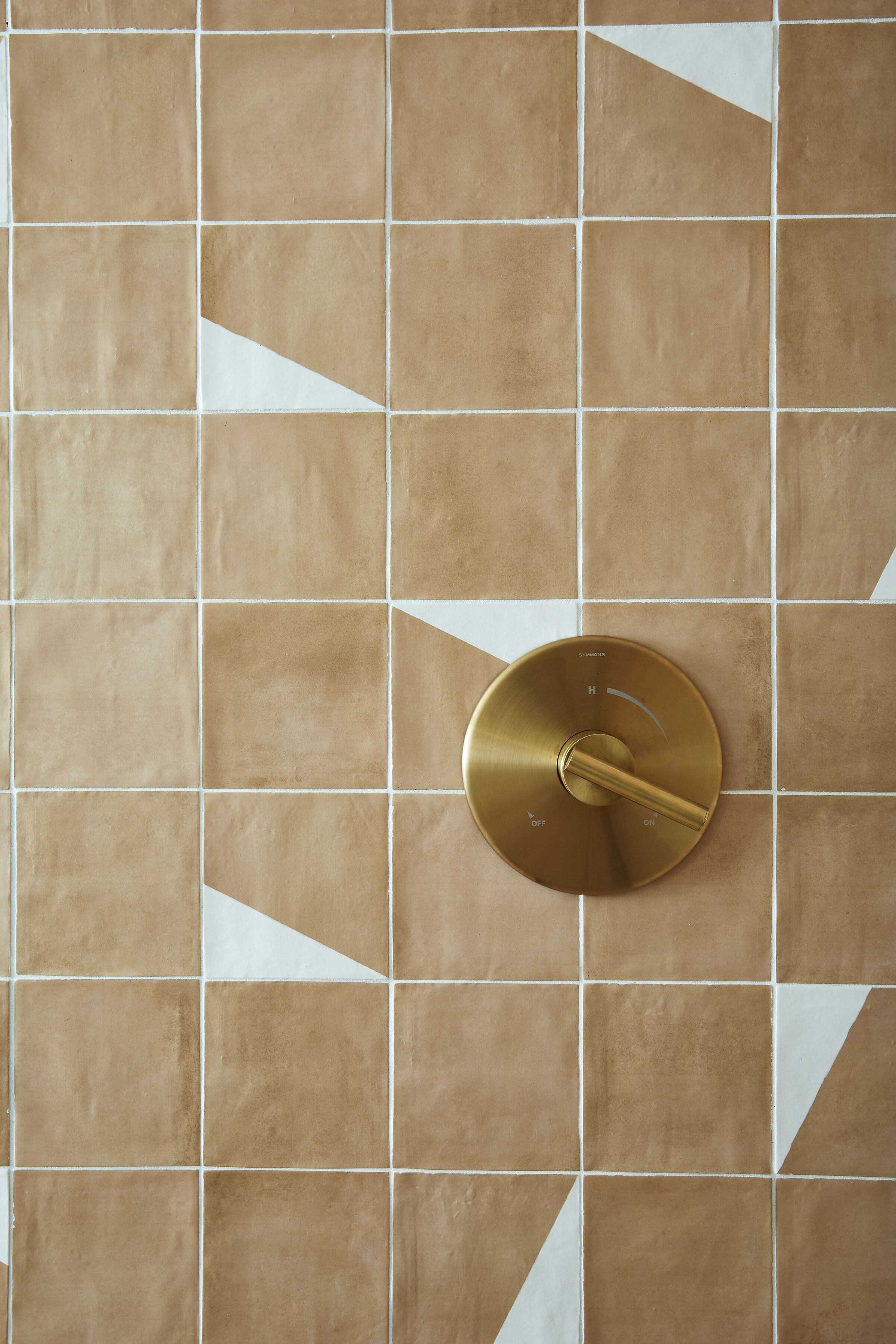 Een badkamer met een betegelde muur en een goudkleurige kraan.