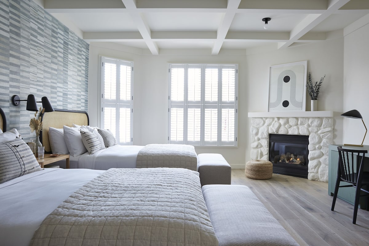 A bedroom with a large bed, two smaller beds, a fireplace, and a view of the outdoors.