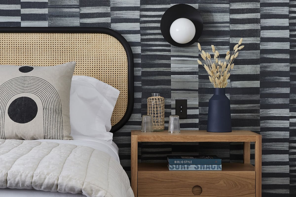 A neatly arranged bedroom with a bed, bedside table, and a wall with a striped pattern.