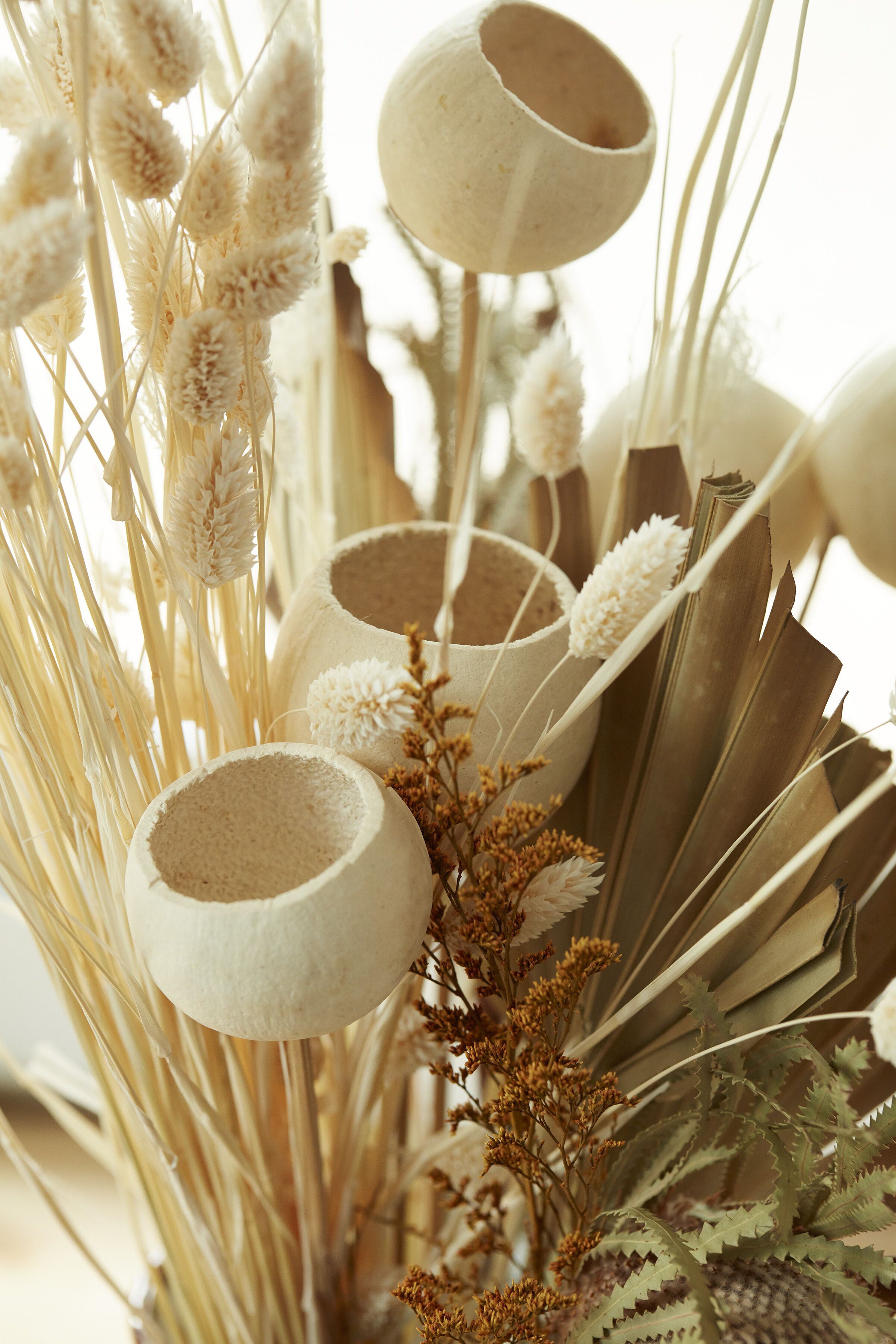 Un dettaglio di una composizione decorativa con piante essiccate e contenitori bianchi e dalla superficie matera.