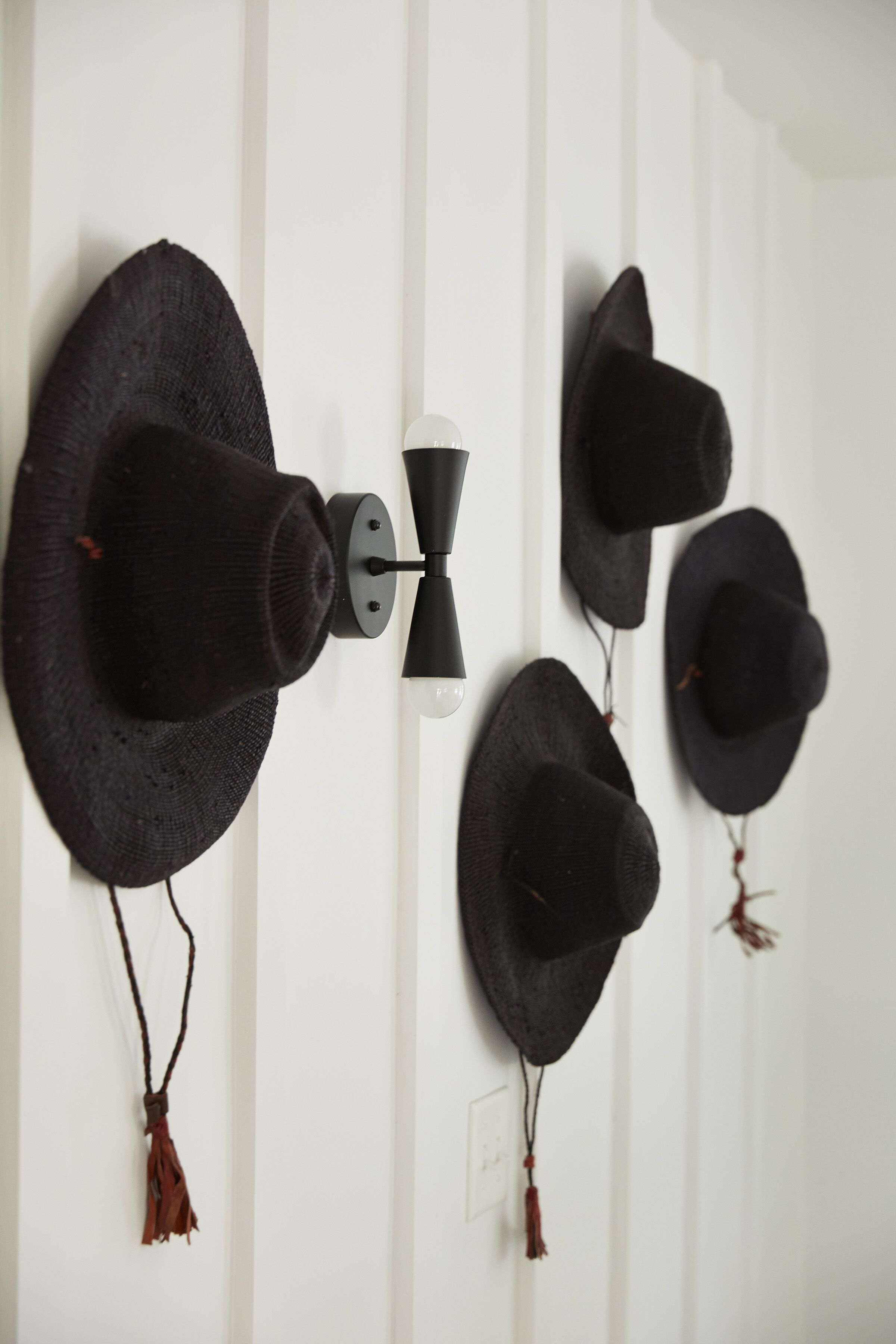 A wall with several black hats hanging on a black metal hook.