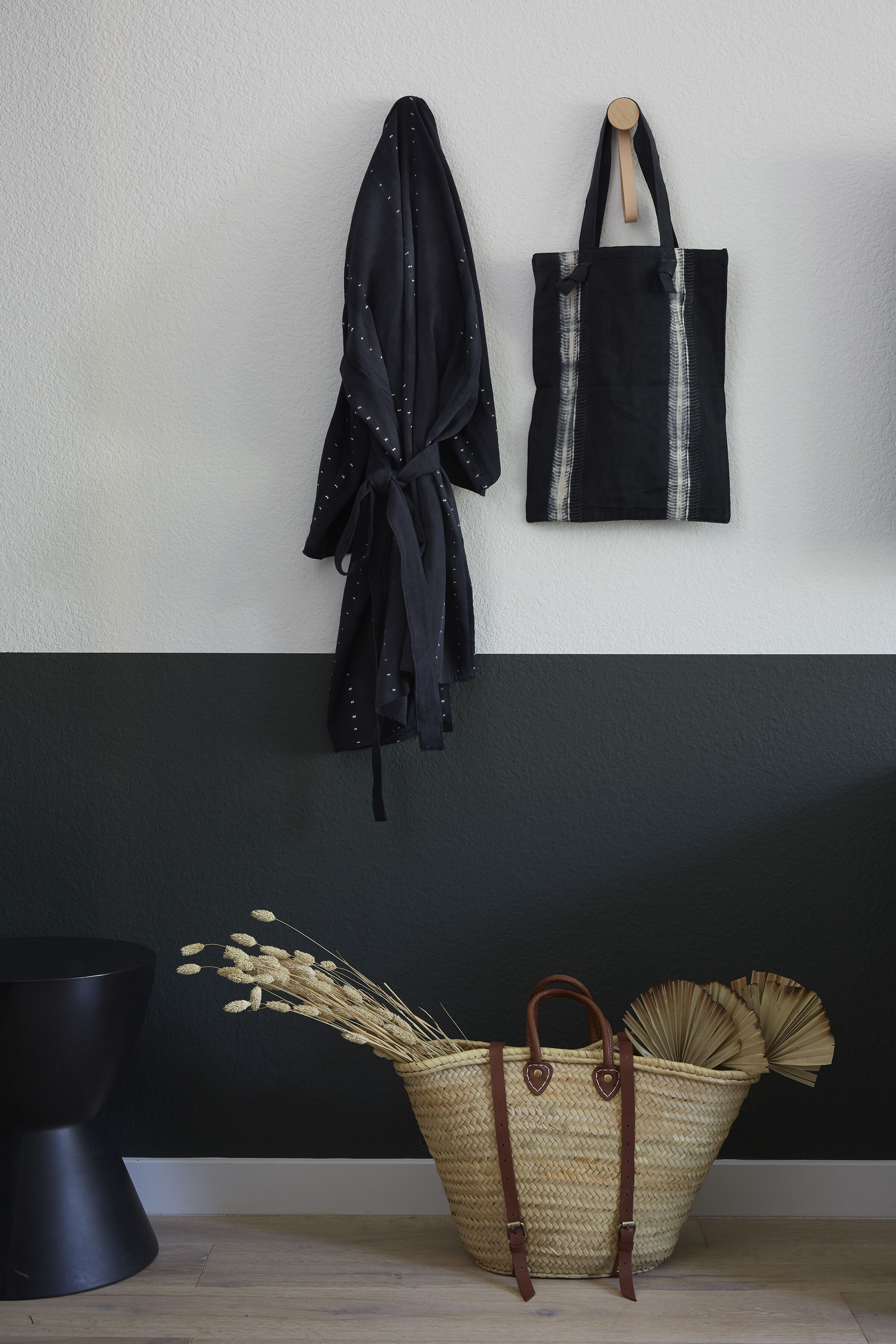 A room with a black and white wall, a black coat, a black bag, and a woven basket with dried plants.