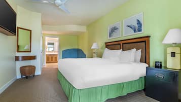 Une chambre d’hôtel avec un lit, une table de chevet, une lampe, une chaise, un miroir et un ventilateur de plafond.