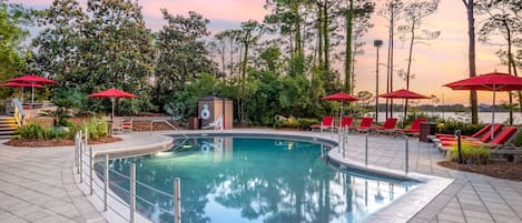 A swimming pool with red umbrellas, lounge chairs, and a small gazebo.