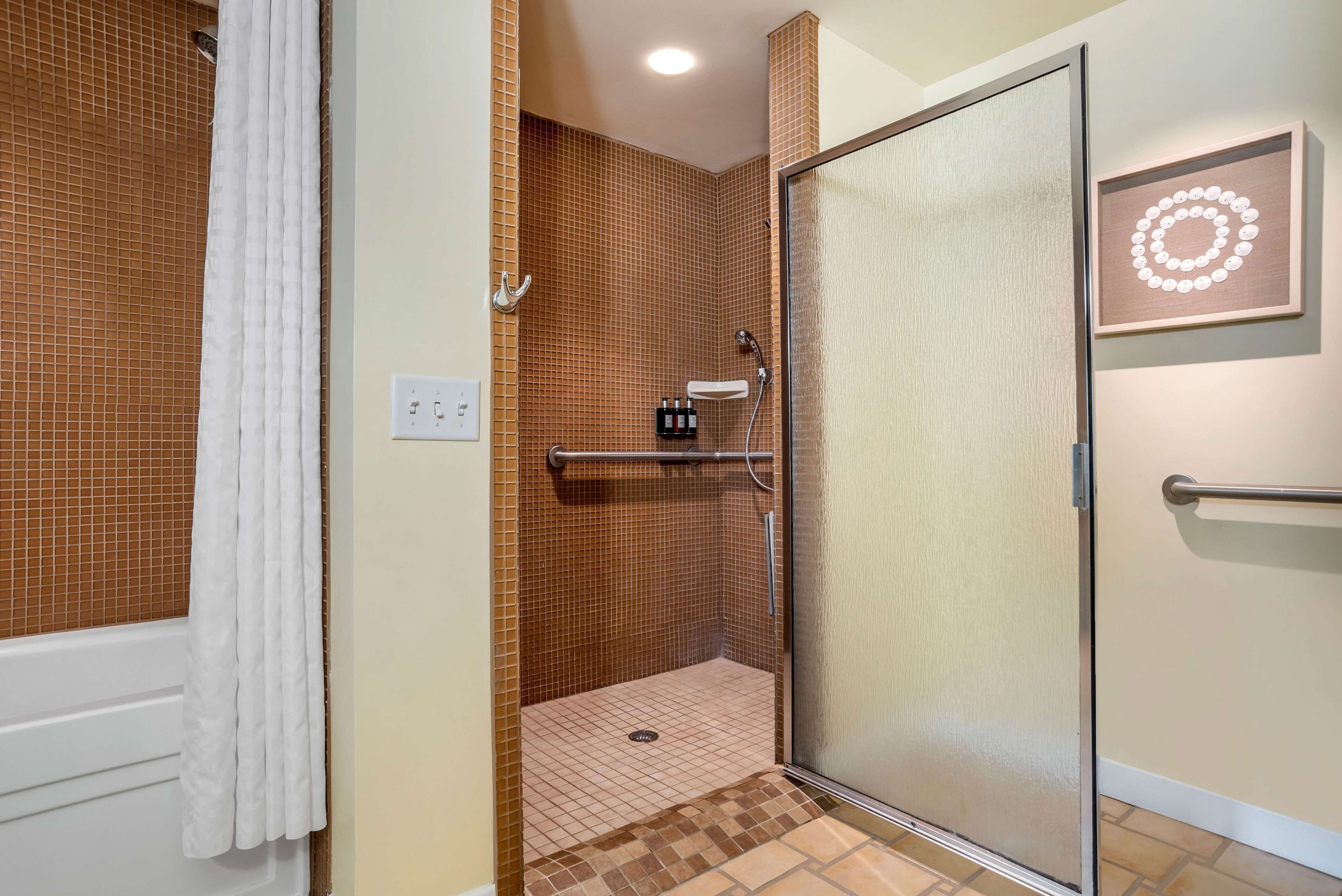 A shower area with a glass door, tiled walls, a white towel, and a shelf with toiletries.