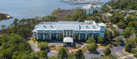 A large, multi-story building with a central dome, surrounded by lush greenery and a marina with boats.