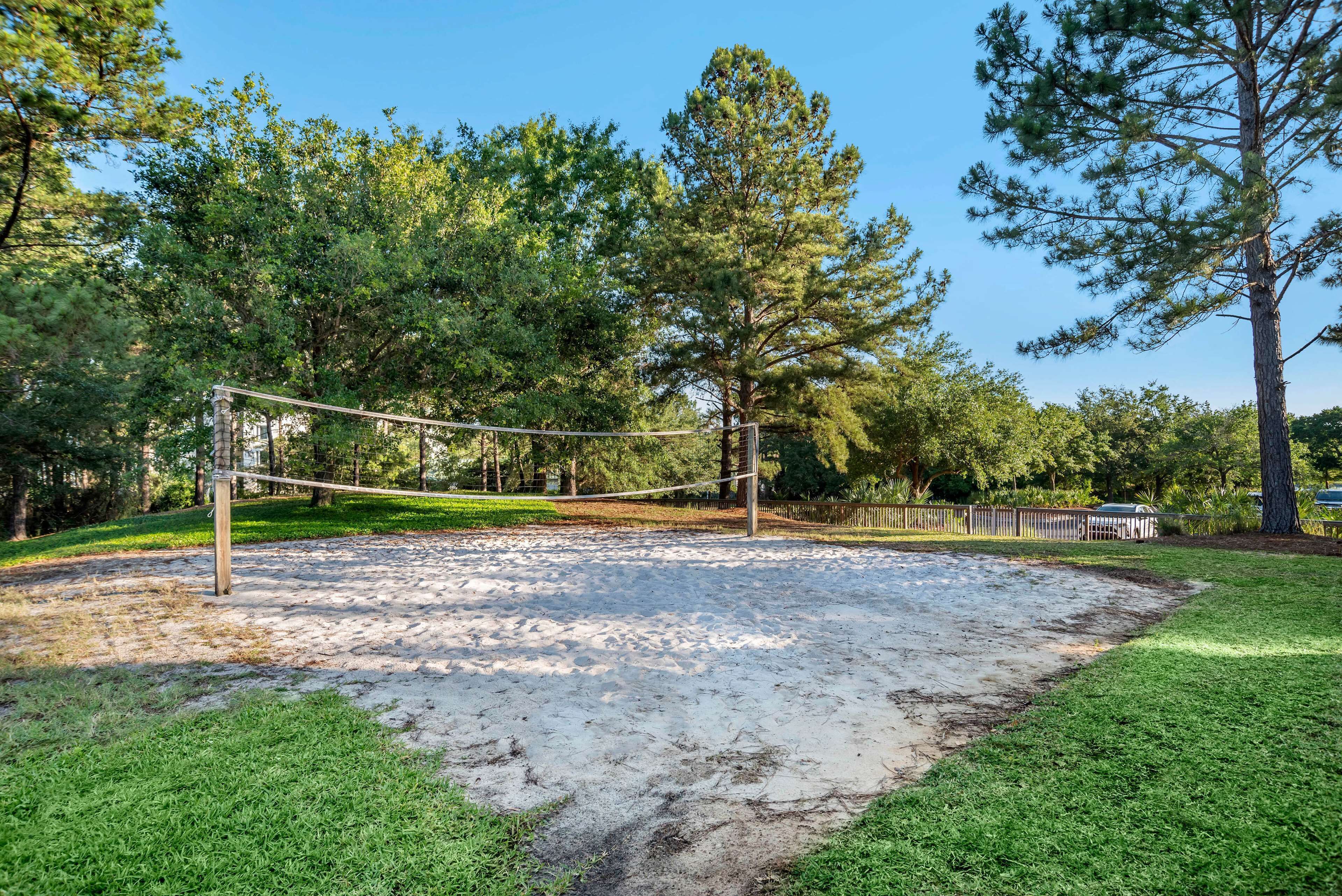 A volleyball court with a net, surrounded by trees and a wooden fence.
