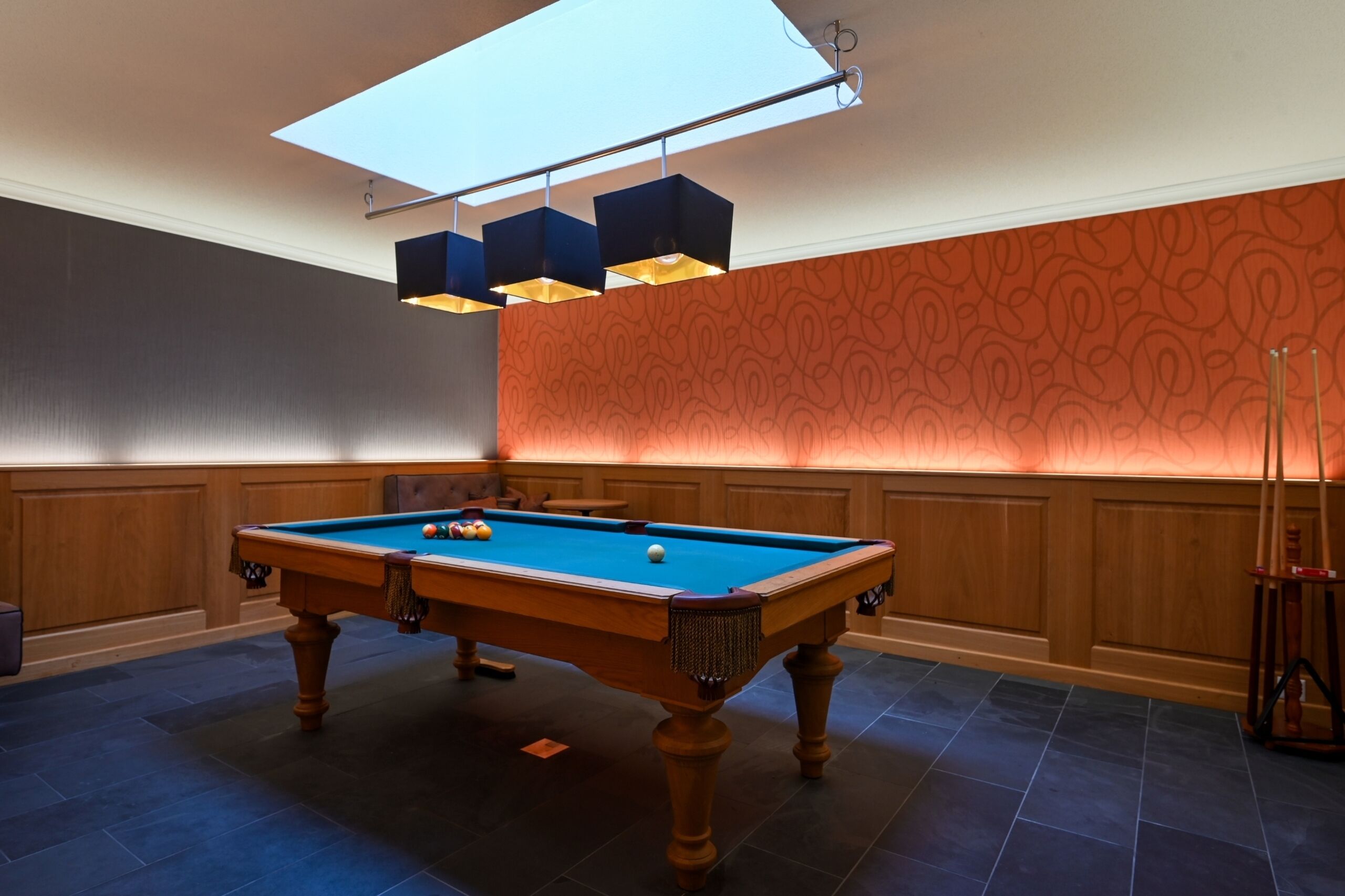 Une table de billard dans une pièce aux murs lambrissés, avec un papier peint à motifs et une lucarne.