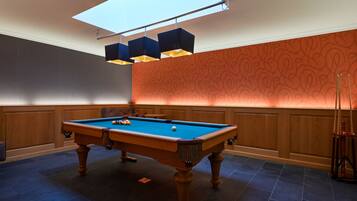 Une table de billard dans une pièce aux murs lambrissés, avec un papier peint à motifs et une lucarne.