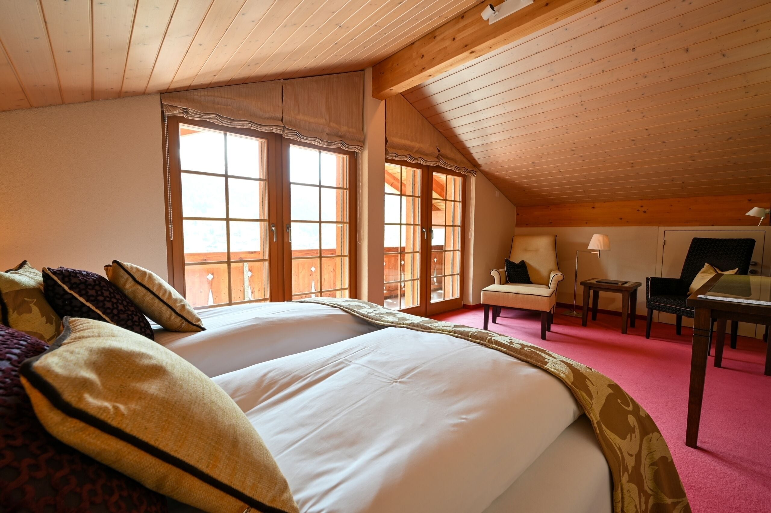 Ein Zimmer mit einem großen Bett, zwei Fenstern, einem Sessel, einem Tisch und einer Lampe.