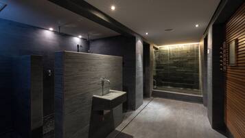 A modern bathroom with dark tiles, a built-in sink, and a glass shower enclosure.