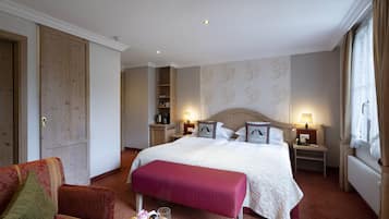 Ett hotellrum med en stor säng, en sittgrupp med en fåtölj, ett litet bord med frukt och ett glas samt en garderob.