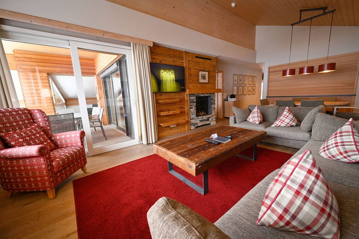 Una sala de estar moderna con chimenea, un conjunto de sofás, una alfombra roja y una mesa de centro de madera.
