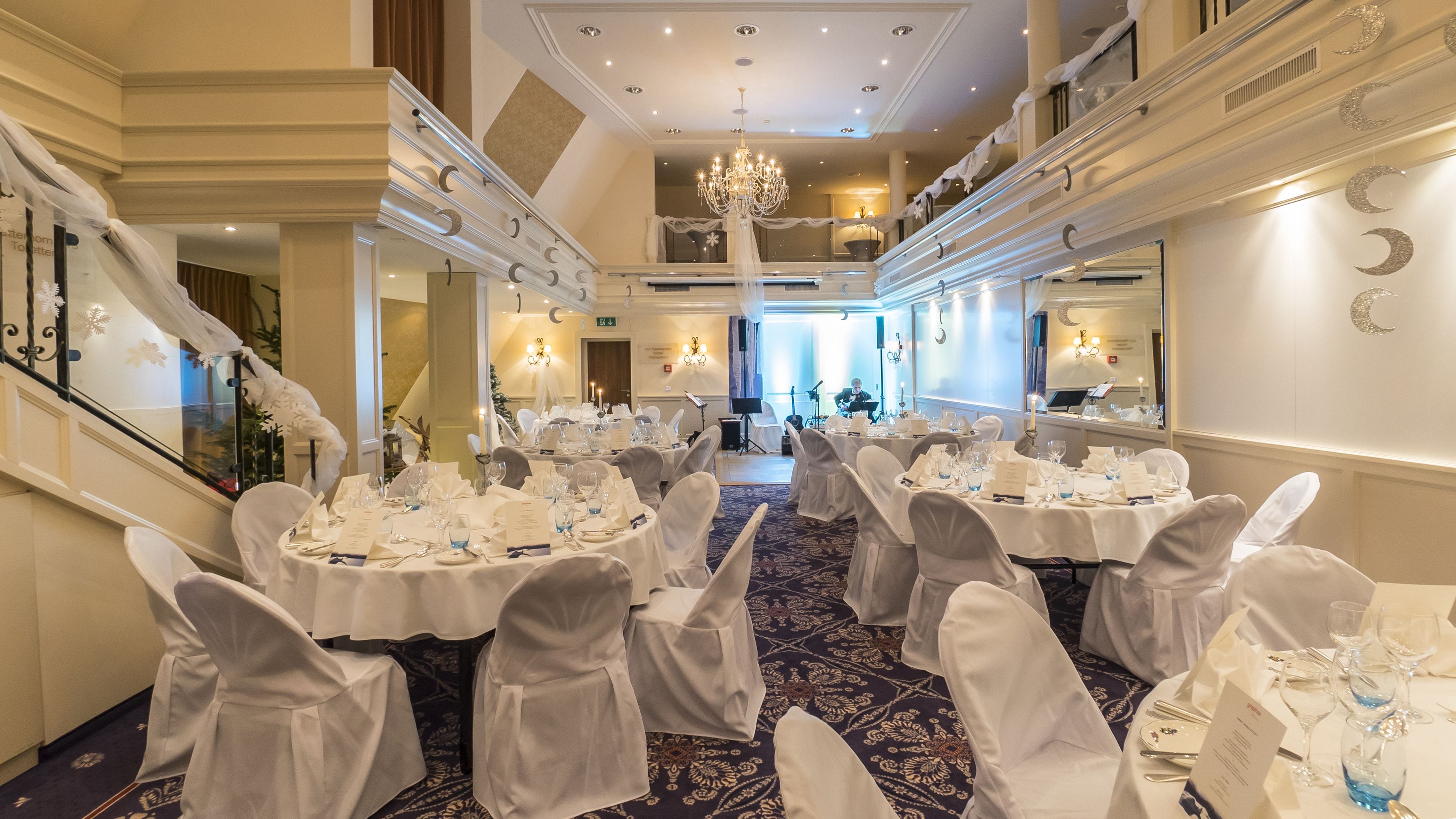 A banquet hall with round tables set for a formal event, featuring chandeliers and elegant decor.