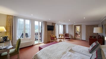 A hotel room with a large bed, a desk with a lamp, a chair, a small table, and a TV.