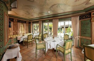 Uma sala de jantar com mesas e cadeiras redondas, esquema de cores verde e bege, e vista para o exterior.
