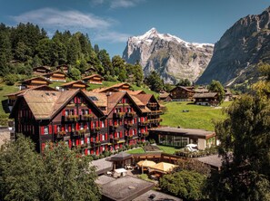 Un hotel de estilo chalete tradicional, con varios balcones, un telón de fondo montañoso y un jardín cuidado.