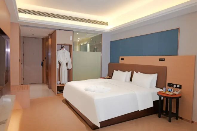 A hotel room with a large bed, a bedside table, a robe hanging on a door, and a shower area.