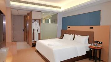A hotel room with a large bed, a bedside table, a robe hanging on a door, and a shower area.