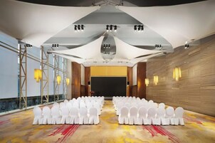 A conference room with rows of white chairs, a stage, and a large screen.