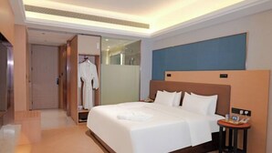 A hotel room with a large bed, a bedside table with a phone and a small table, a wardrobe, and a mirror. - Mingxing Conifer Hotel (Suining)