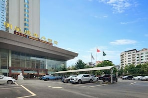 A hotel with a modern facade, a covered entrance, and a parking lot with several cars.