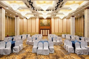 A conference room with rows of tables and chairs, a large chandelier, and a painting on the wall.