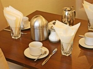 A neatly arranged dining table with a coffee pot, cups, and a sugar bowl.