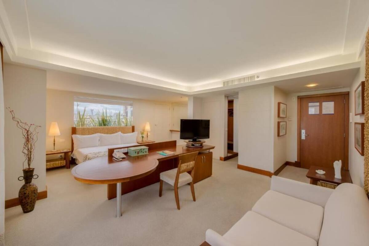 A modern hotel room with a bed, a desk with a chair, a television, and a sofa.