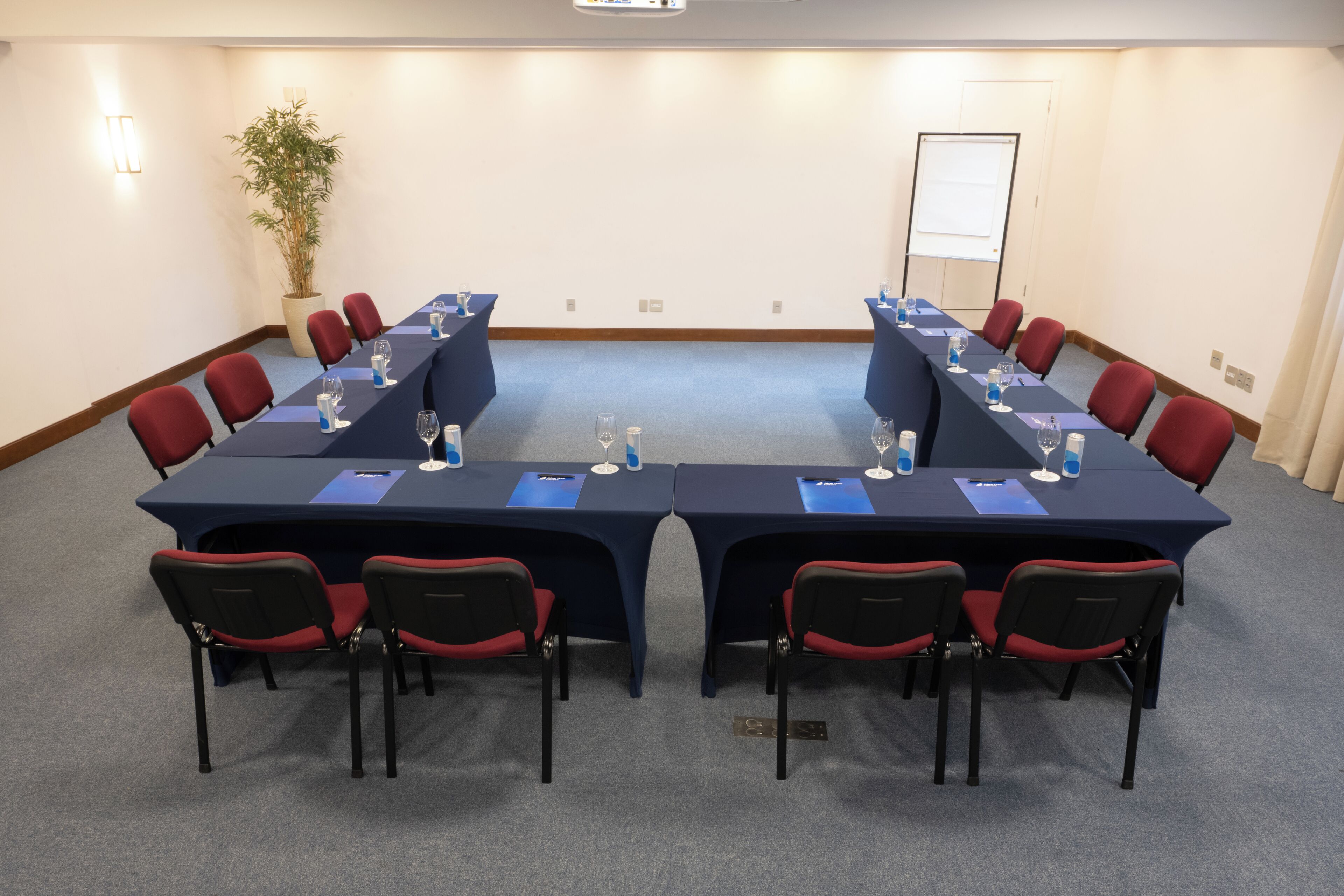 Ein Konferenzraum mit langem Tisch, roten Stühlen und einer Zimmerpflanze.