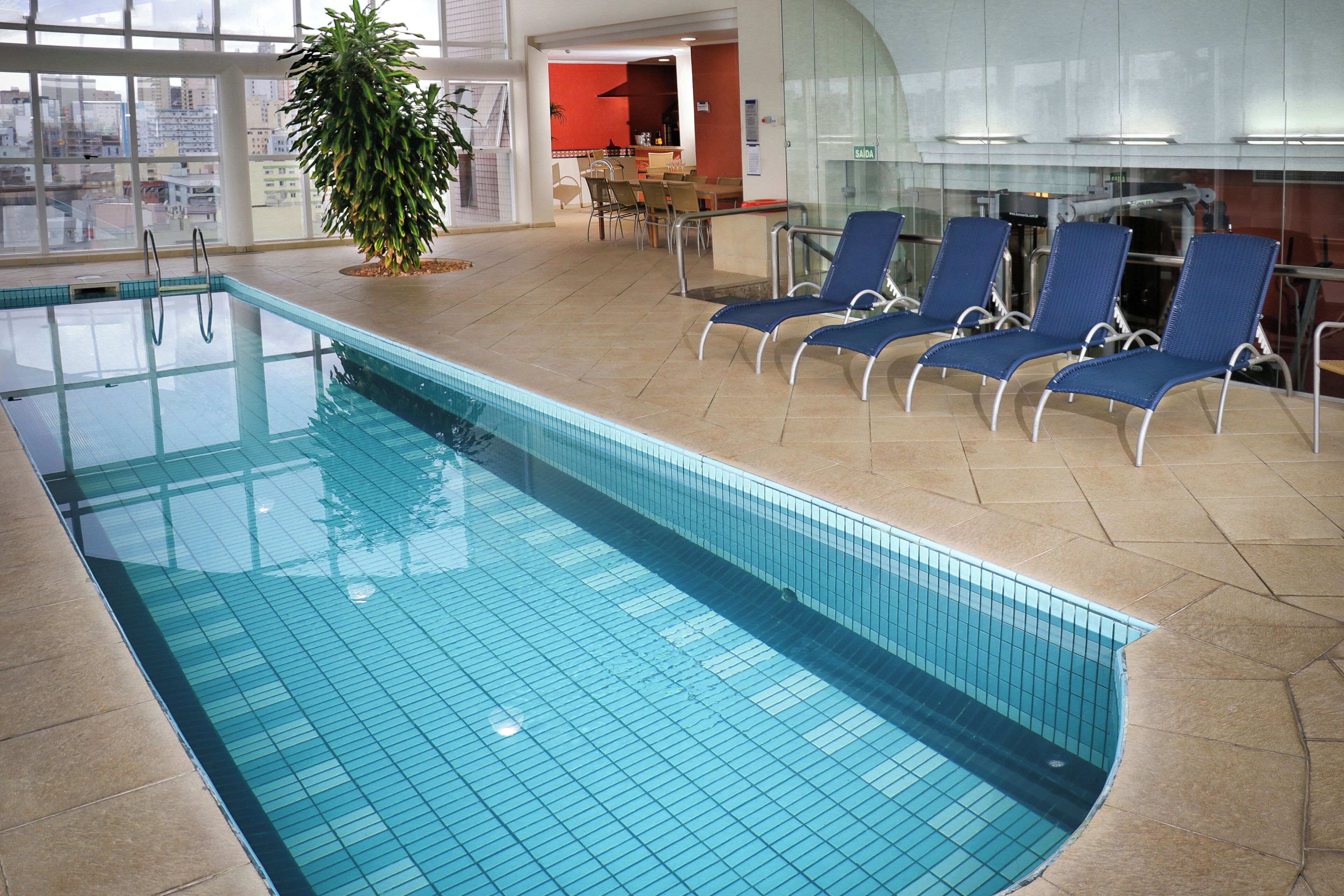 An indoor swimming pool with clear blue water, surrounded by lounge chairs and a potted plant.