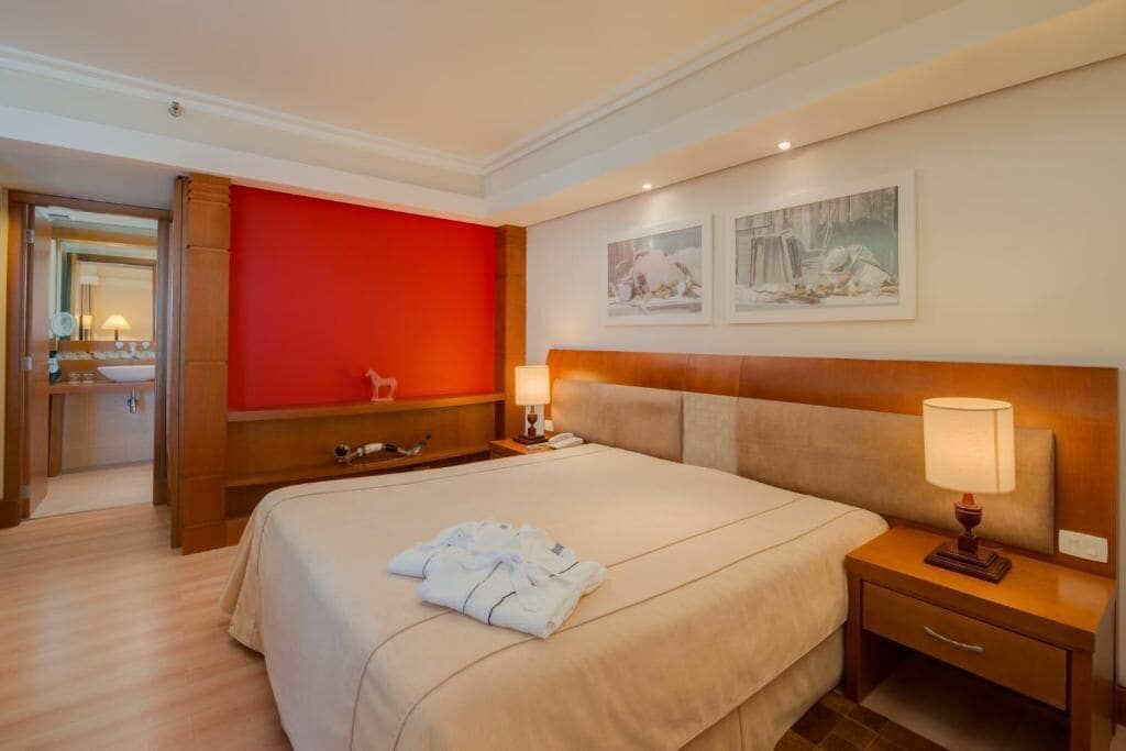A hotel room with a large bed, a wooden headboard, a red accent wall, and two framed artworks.