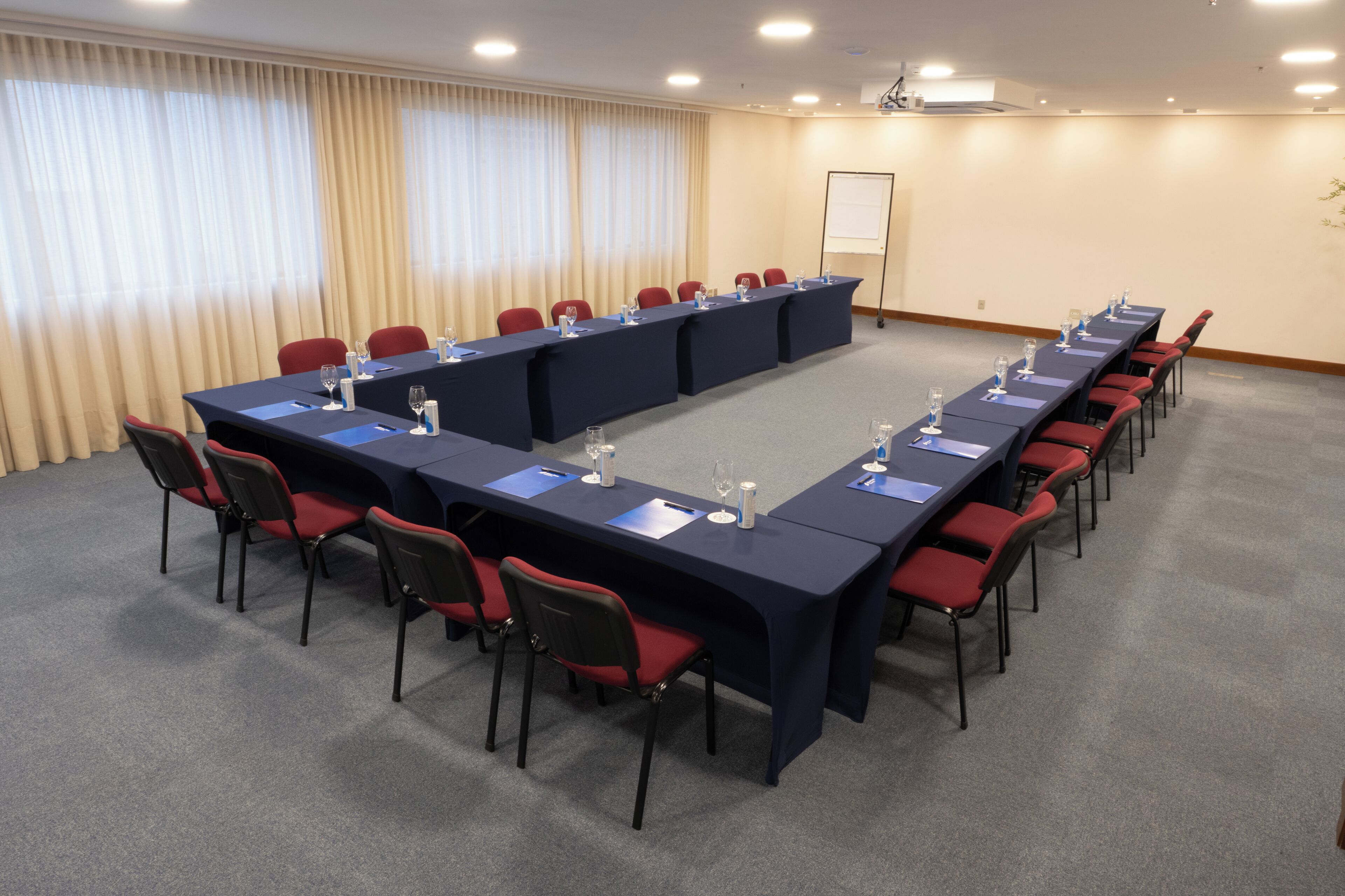 A conference room with a long table, red chairs, and a projector screen on the wall.