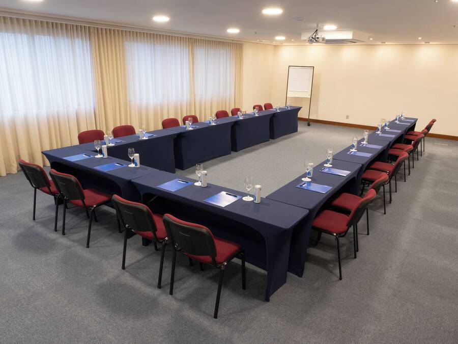 A conference room with a long table, red chairs, and a projector screen on the wall.