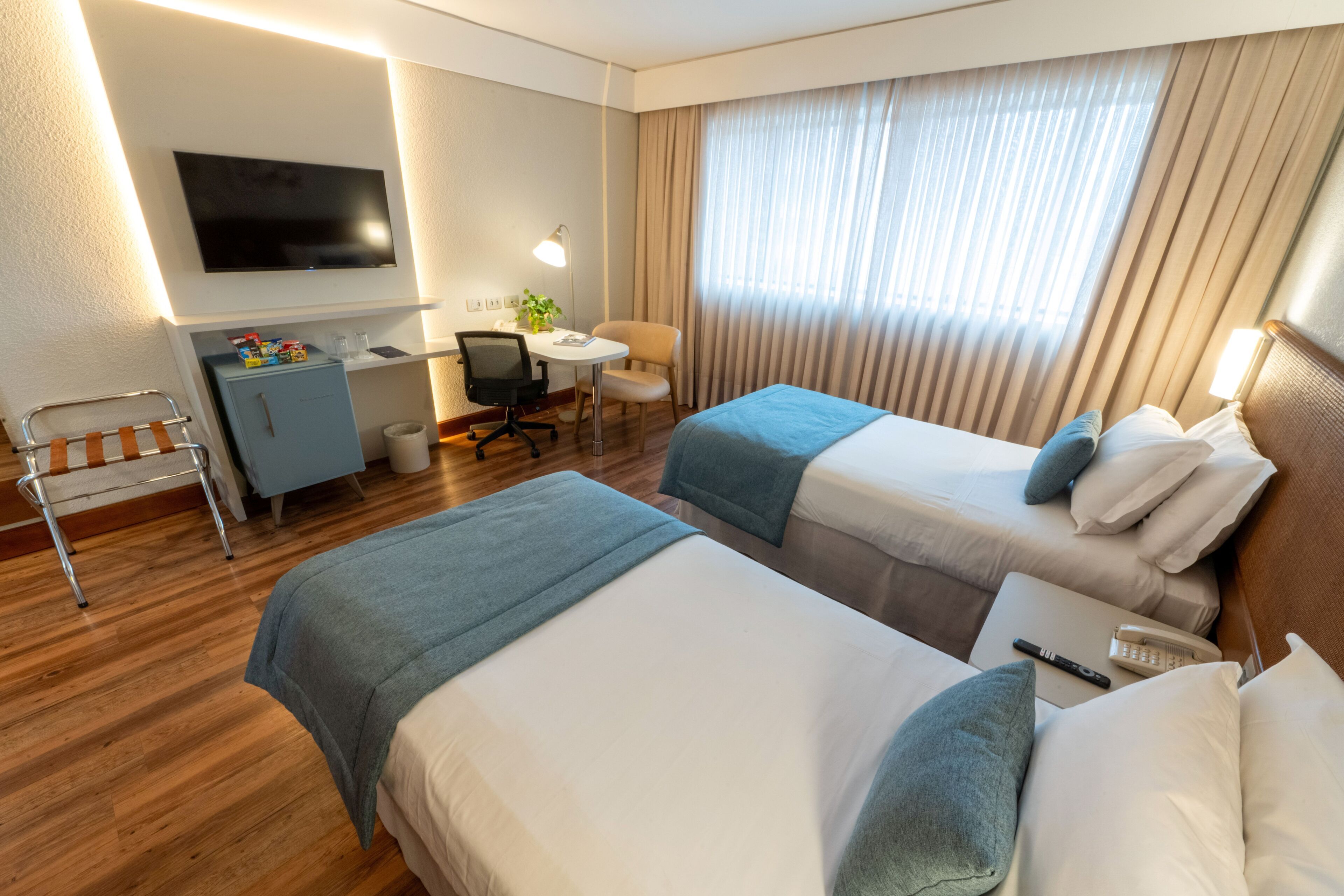 Een hotelkamer met twee bedden, een bureau, een stoel, een televisie en een raam met gordijnen.