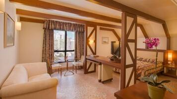 Um quarto de hotel acolhedor com teto de madeira, uma mesa com cadeira, uma televisão, uma cama com colcha estampada e um vaso de planta.