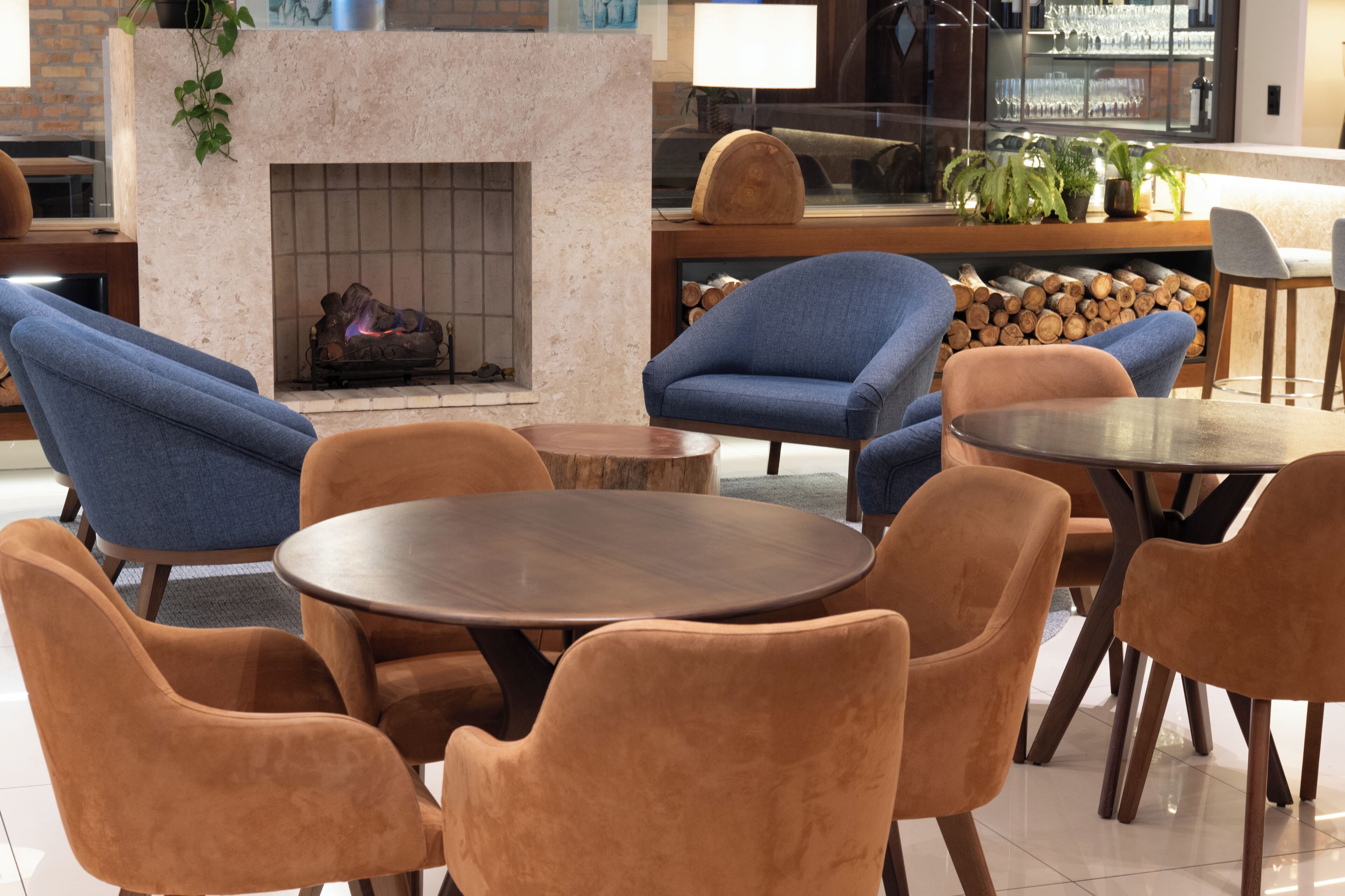 A modern lounge area with a fireplace, comfortable seating, and a bar area with plants and a log display.