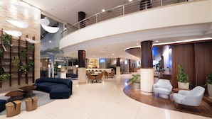 A spacious lobby with a curved ceiling, a seating area with sofas and chairs, a reception desk, and a staircase leading to an upper level. - Blue Tree Towers Caxias do Sul (Caxias do Sul)