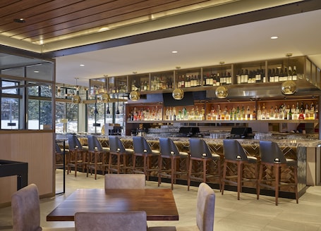 A modern bar area with a long counter, multiple seating options, and a variety of bottles and glasses on display.. Limelight Hotel Aspen