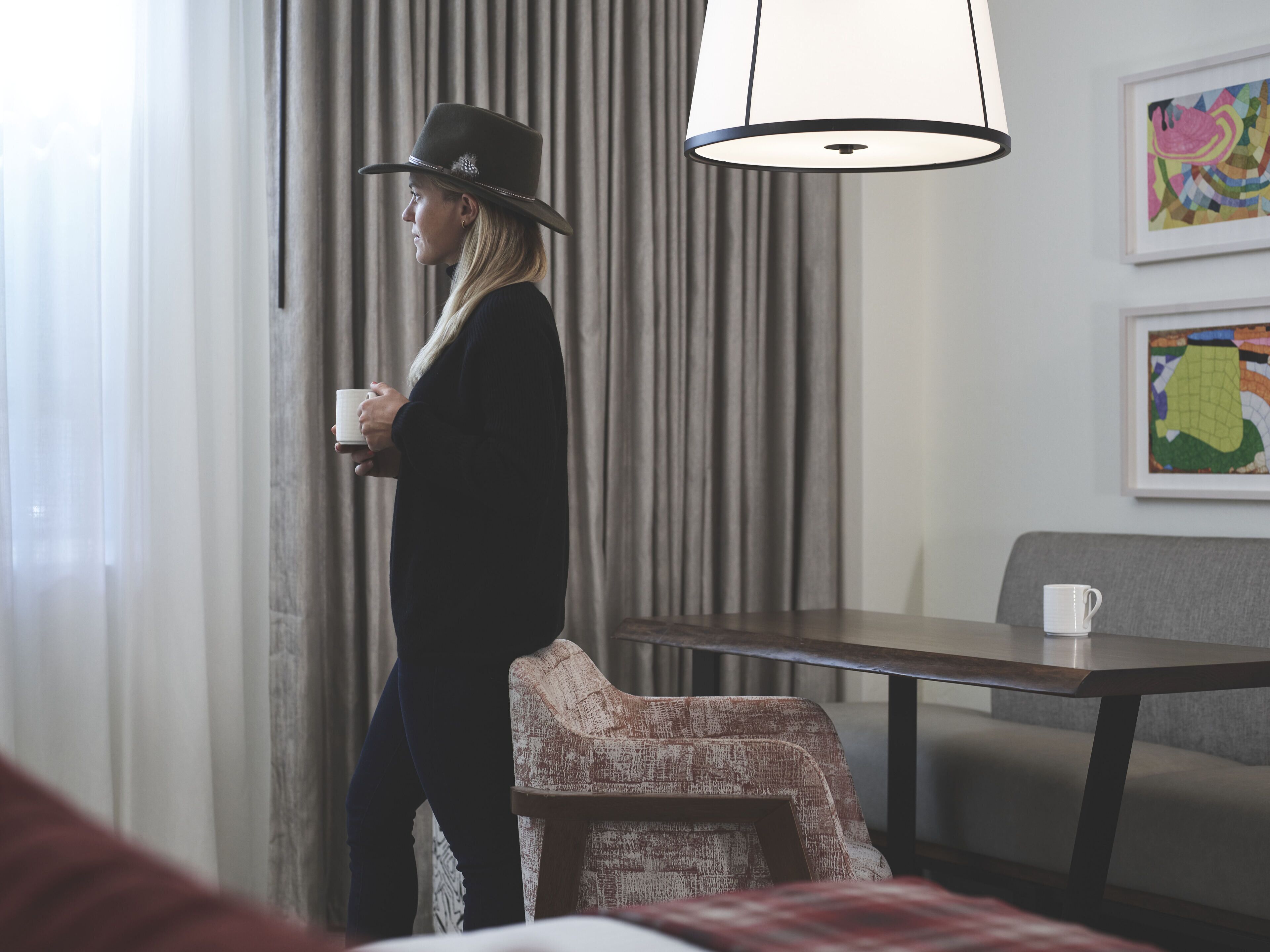Quarto de hotel com uma cama, uma cadeira, uma mesa e uma janela grande com cortinas.
