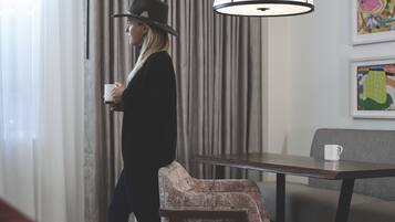 Una habitación de hotel con cama, una silla, una mesa y un ventanal con cortinas.