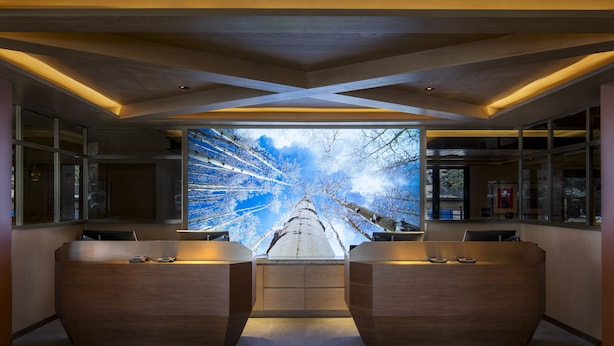 Zona de recepción con una gran pantalla digital, mostrador de madera y vista a un paisaje nevado a través del ventanal.