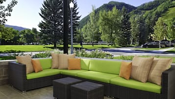 Un sofá modular con cojines verdes y almohadones estampados, una mesita y vistas a un parque y montañas.