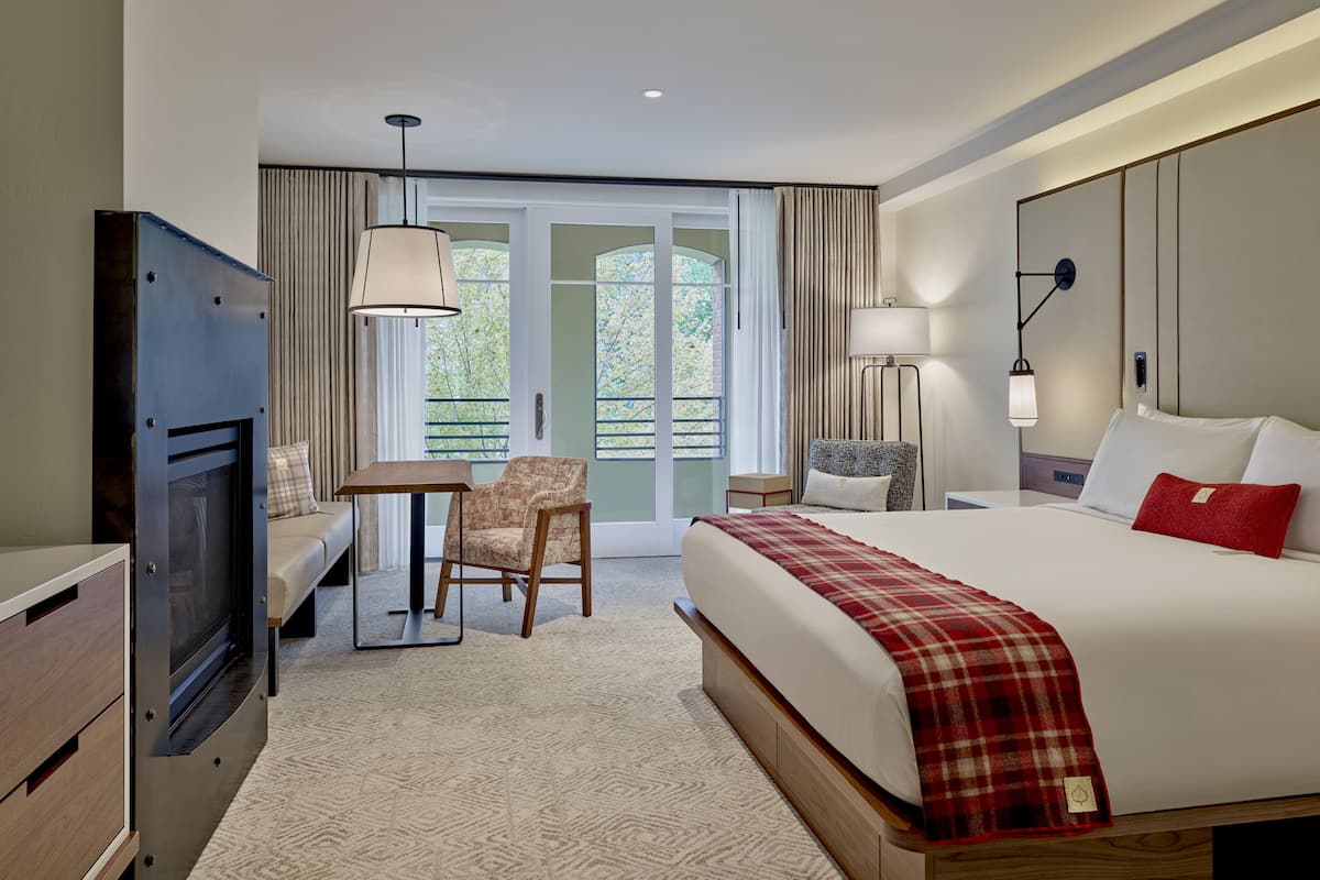 Quarto de hotel com cama, televisão, escrivaninha, cadeira, abajur e vista para o exterior.