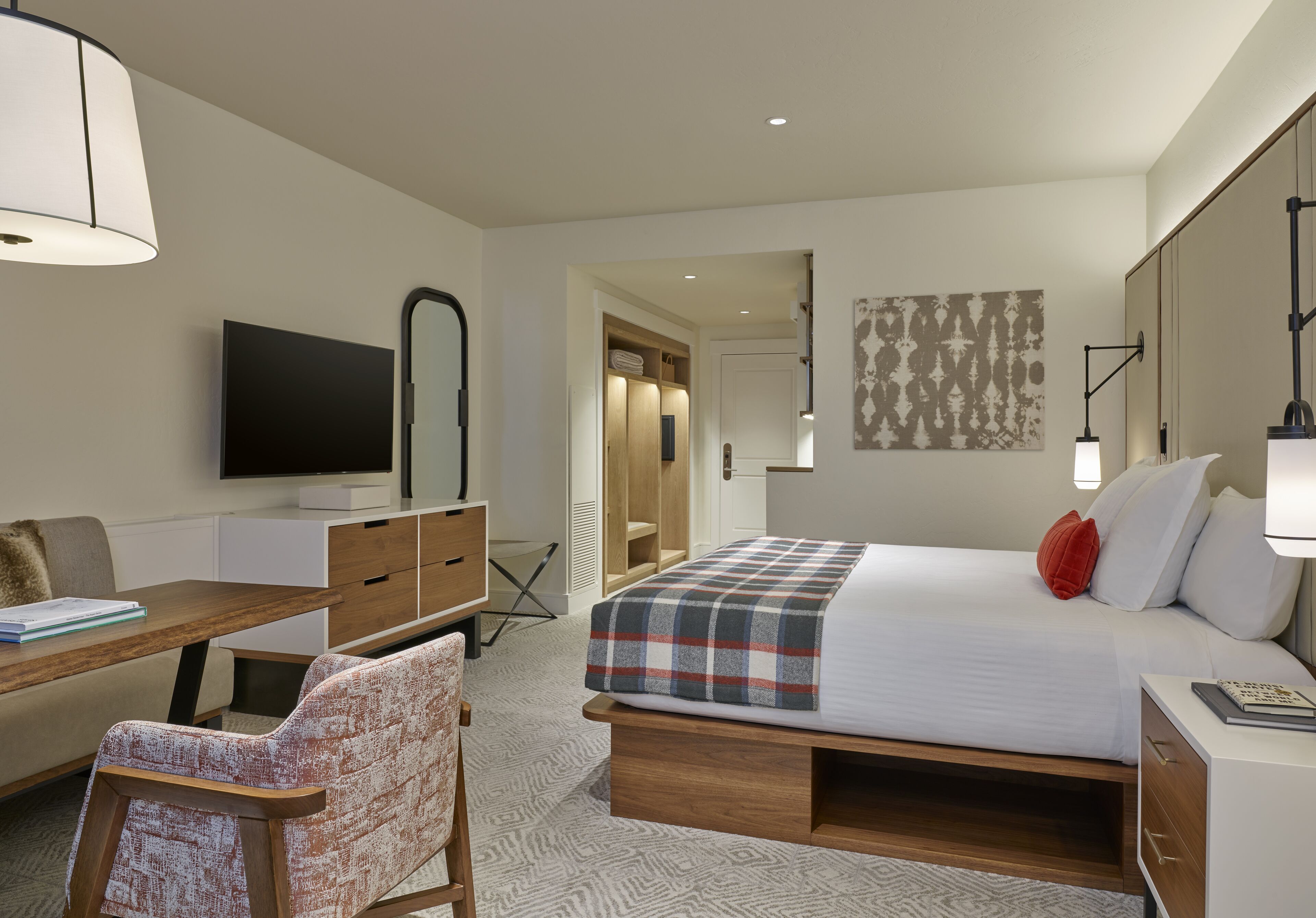 A hotel room with a bed, a desk, a chair, a television, and a wardrobe.